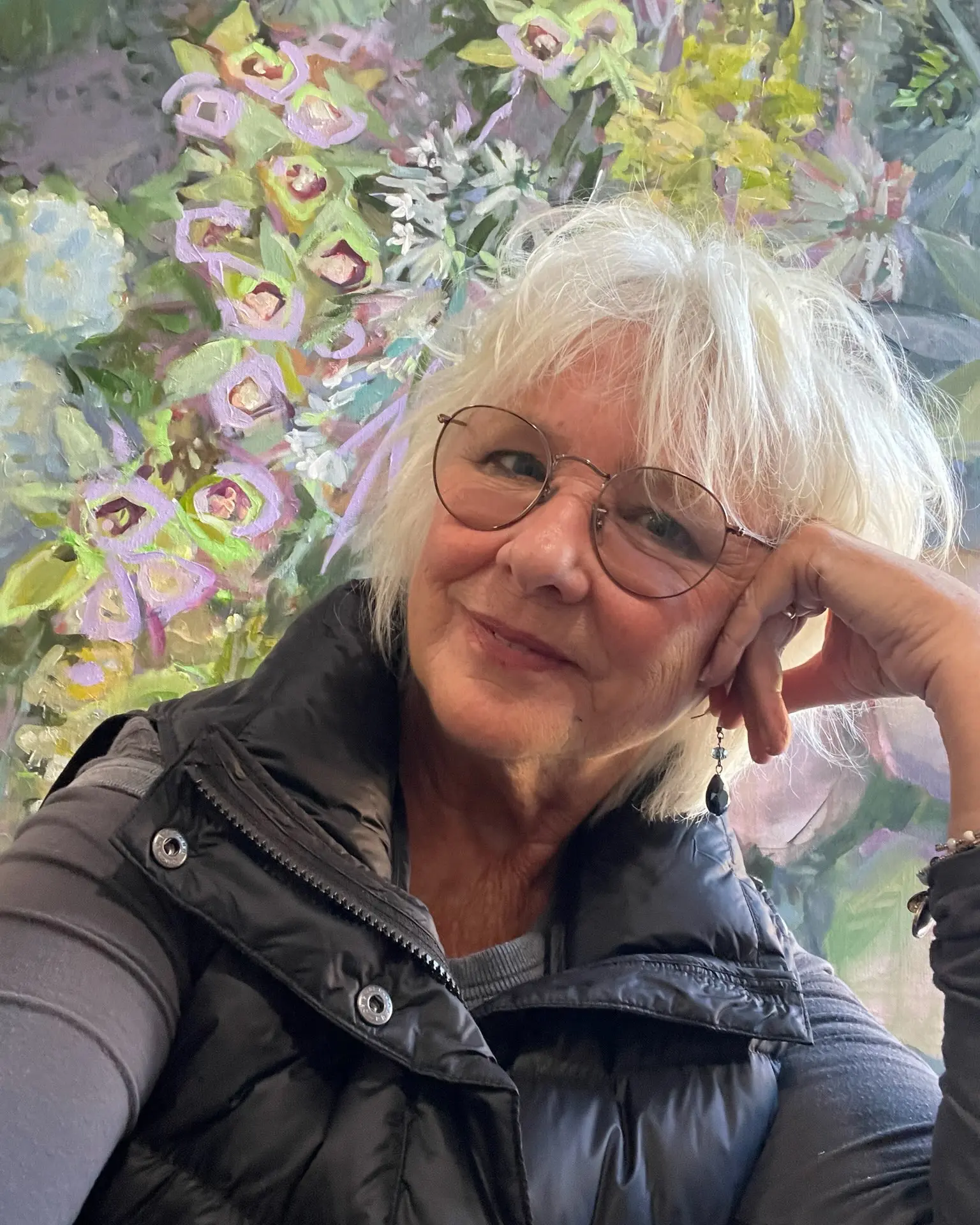 Sandra Gittleman, Fine Art Painter, smiling while seated in front of her floral impressionist painting.